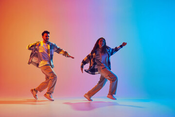 Two joyful dancers in motion, man and woman in neon colorful lighting against gradient background. Concept of movement, energy, dance battles. Dynamic gel portrait