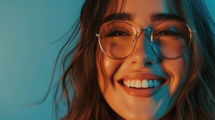 Fototapeta premium A close-up of a smiling woman with glasses set against a blue background showcasing her radiant smile and the warmth of her eyes.