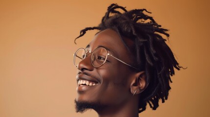 Smiling man with glasses and dreadlocks against a warm background.