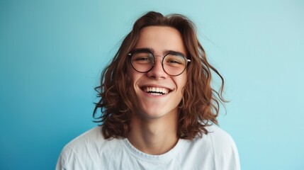Fototapeta premium Young man with long curly hair wearing glasses smiling at the camera against a blue background.