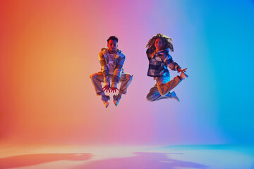Energetic positive pair, dancers leaping in neon colorful illumination suspended in mid-air against...