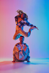 Dance duet. Woman jumps over man crouching in radiant neon glow. Dynamic dance move and joyful...