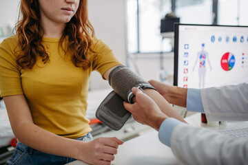 Doctor examining teenage girl, measuring blood pressure, using clinical blood pressure monitor....