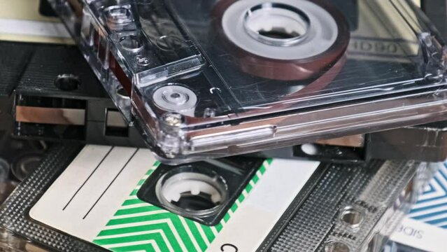 Many different audio cassettes stacked in a heap rotate on a wooden table close-up. Different vintage audio tapes spin. Old audiocassettes lying in macro. Classic, retro music, 80s, 90s. Nostalgia.