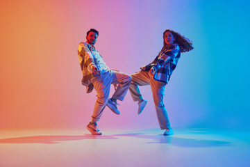 Full-length portrait of dancers connect mid-step in motion in vivid lighting against gradient...