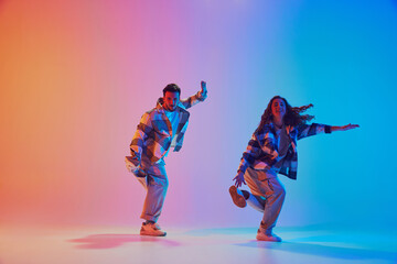 Full length portrait of hip-hop dancers performing in motion against gradient studio background. Synchronized movements. Concept of fashion and style, energy, dance battles. Dynamic gel portrait