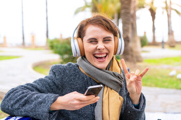 Brunette woman at outdoors listening music with a mobile making rock gesture
