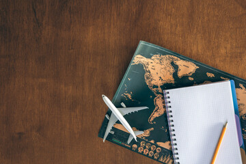 World map, airplane miniature and notepad on a wooden table, top view.