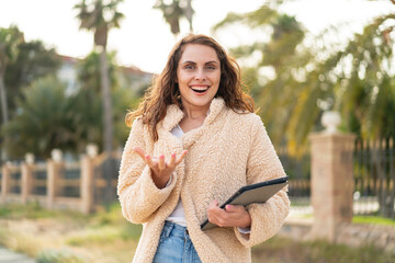 Young caucasian woman holding a tablet at outdoors with shocked facial expression