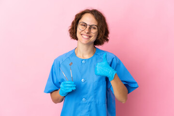 Woman English dentist holding tools over isolated on pink background giving a thumbs up gesture