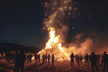 Crowd of people stands around majestic bonfire reaching dark sky at night. Celebration of old holiday by whole village. Lighting fire for rituals, close-up - obrazy, fototapety, plakaty