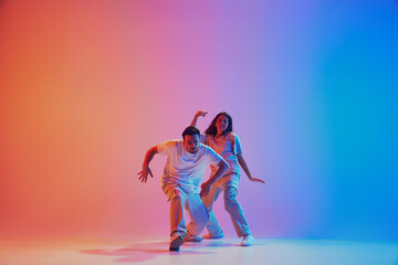 Dynamic lifestyle. Dancers performing hip hop, freestyle in neon lights against gradient studio background. Concept of youth culture, style, movement, energy, dance battles, hobby. Gel portrait