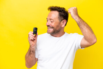 Middle age caucasian man holding car keys isolated on yellow background celebrating a victory