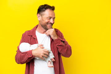 Middle age caucasian man holding his newborn son isolated on yellow background thinking an idea and...