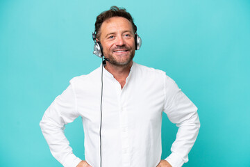 Telemarketer caucasian man working with a headset isolated on blue background posing with arms at...