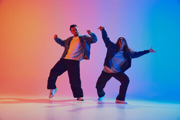 Male and female dancer in sync dressed casual urban wear against gradient background in neon light, filter. Concept of youth culture, music, lifestyle, style and fashion, action. Gel portrait.