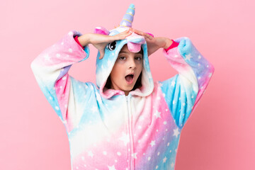 Little caucasian woman wearing a unicorn pajama isolated on pink background with surprise expression