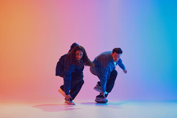 Two dancers performing sync hip-hop moves dressed in denim clothes against gradient background in...