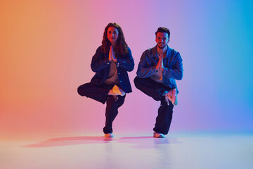 Dance duo, talented man and woman in dance poses against gradient studio background in neon light, filter. Concept of youth culture, music, lifestyle, style and fashion, action. Gel portrait.