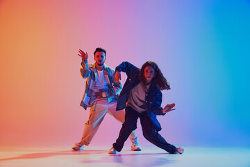 Dynamic lifestyle. Man and woman, hip-hop dance moves sync in motion against gradient studio background in neon light. Concept of youth culture, music, style and fashion, action. Gel portrait.