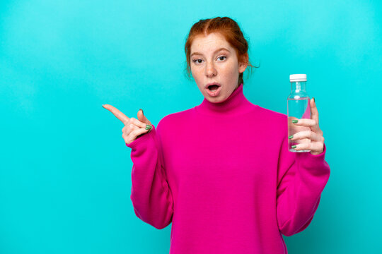 Young caucasian reddish woman with a bottle of water isolated on blue background surprised and pointing side