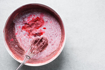 Top view of buttermilk being mixed into Red velvet cake batter in white ceramic mixing bowl, process of making red velvet cake