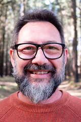 Fototapeta premium Cheerful adult happy man taking selfie picture in the woods enjoying outdoors leisure activity in national forestal park alone. Adventure and lifestyle people. High trees in background. Sustainability