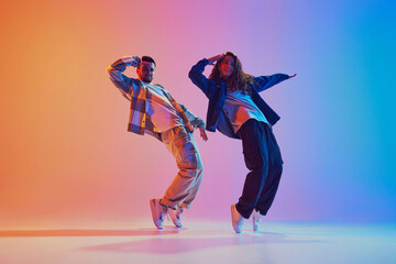 Urban lifestyle. male and female, young dancers against gradient blue-orange background in neon...