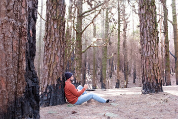 Fototapeta premium One man using phone cellular connection in a forest wood enjoying technology and outdoor leisure activity. Modern man speaking at cellular with trees in background. People and communication on travel