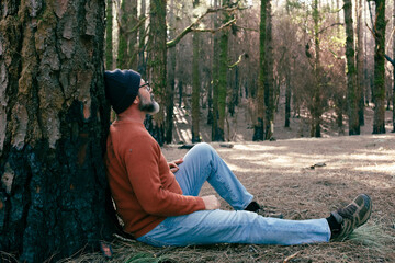 One man having relaxation time sitting on the ground in the middle of green forest woods and...