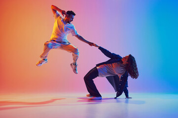 Dynamic photo of man leaping, woman bending backwards against vivid pink-blue gradient background. Energetic dance pose. Concept of youth culture, music, style, fashion, action. Gel portrait.