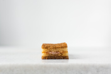 A slice of vanilla cake with jam filling, thin layers of vanilla and chocolate cake with jam filling on a white background