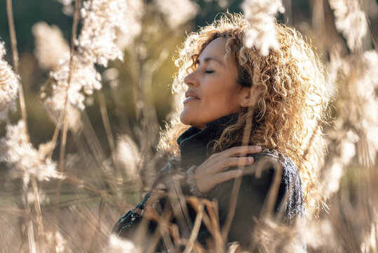 One woman in love for nature. Sustainability and environment concept people lifestyle. Curly female hugging herself in a golden field of grass in sunset light. People in outdoor leisure activity life