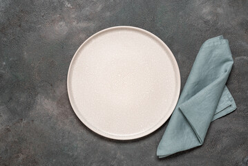 Empty beige plate mockup with blue linen napkin, dark grunge background. Top view, flat lay....
