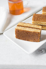 A slice of vanilla cake with jam filling, thin layers of vanilla and chocolate cake with jam filling on a white background