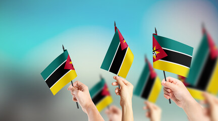 A group of people are holding small flags of Mozambique in their hands.