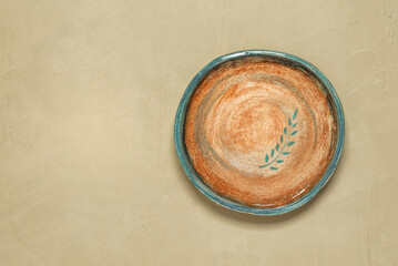Empty vintage handmade plate with pattern, beige plaster background. Top view, flat lay, copy space.