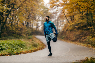 A fit sportsman is stretching his leg while exercising in nature.