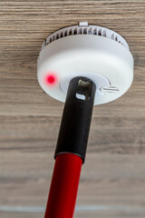 Checks smoke detector with a cleaning broom