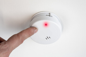 Finger testing smoke detector mounted on ceiling