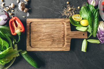 Cutting board and fresh vegetables on a black kitchen table, top view.