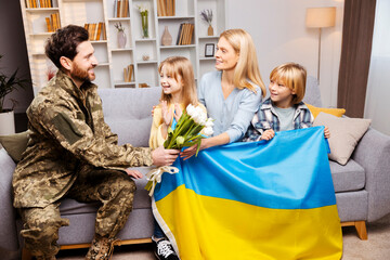 Father in military gear gifts his wife flowers, while their kids hold Ukrainian flag