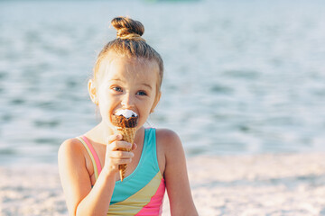 Happy little blonde girl in a bathing suit eating an ice cream. High quality photo