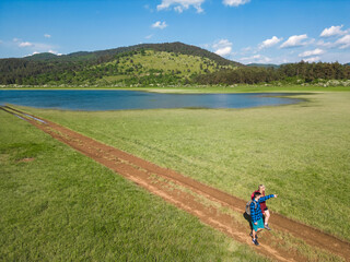 Hiking couple enjoy walking along a trail near blue mountain lake, exploring beautiful nature on a sunny summer day, aerial view. Outdoors recreation concept.