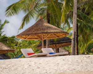 Wooden beach parasol and beach loungers at sunset.Luxury beach parasol at luxurious beach resort. Summer beach concept,carefree, rest seaside,Nobody on the beach.Palm on the back.