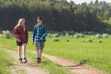Two adolescents, a girl, and a boy, walk, explore, and enjoy the beauty of the countryside nature on a sunny day. Teenagers and outdoor activity concepts.