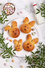 Buns made from yeast dough in a shape of Easter bunny, and colored candy eggs. Traditional Easter symbols and food. Top view