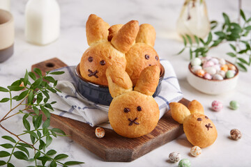 Buns made from yeast dough in a shape of Easter bunny, and colored candy eggs. Traditional Easter symbols and food. Selective focus.