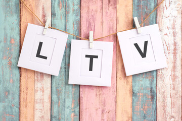 three blank white sheets of square format paper with text LTV hang from a rope with clothespins on multicolored background