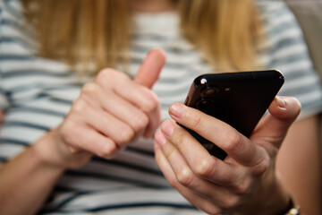 Woman using mobile phone at home. Female sitting on sofa and browsing social networks on smartphone